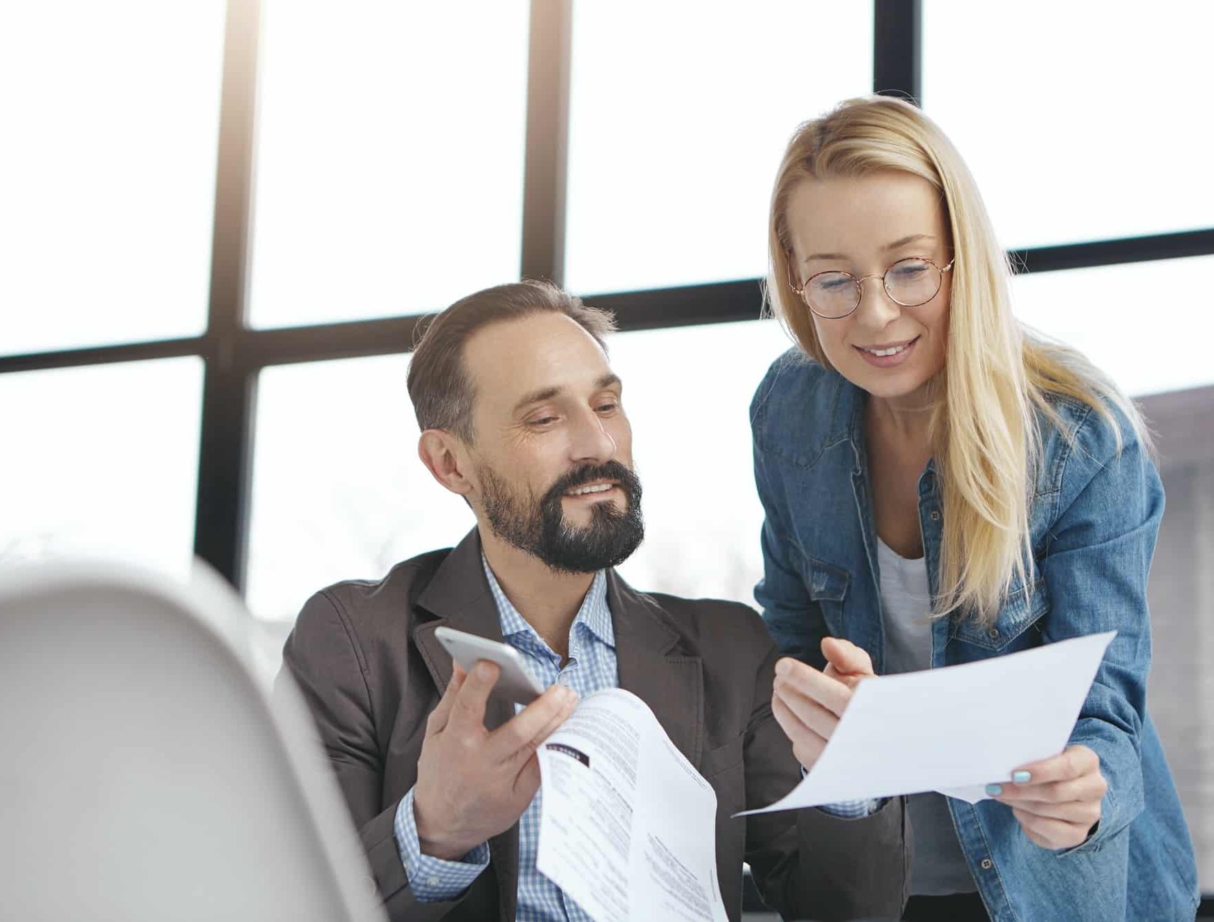 Positive young female with blonde hair, wears fashionable denim shirt, get consultancy from experien